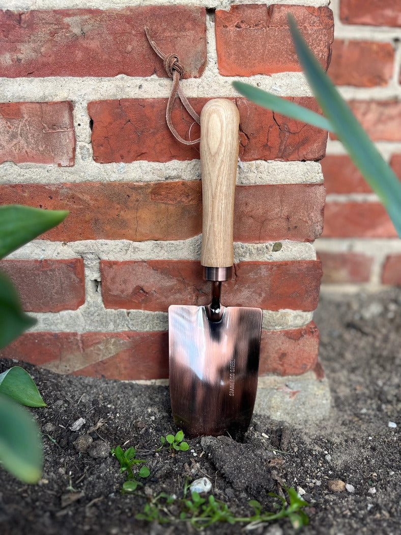 Kobber haveskovl med træhåndtag, der står op ad en murstensmur