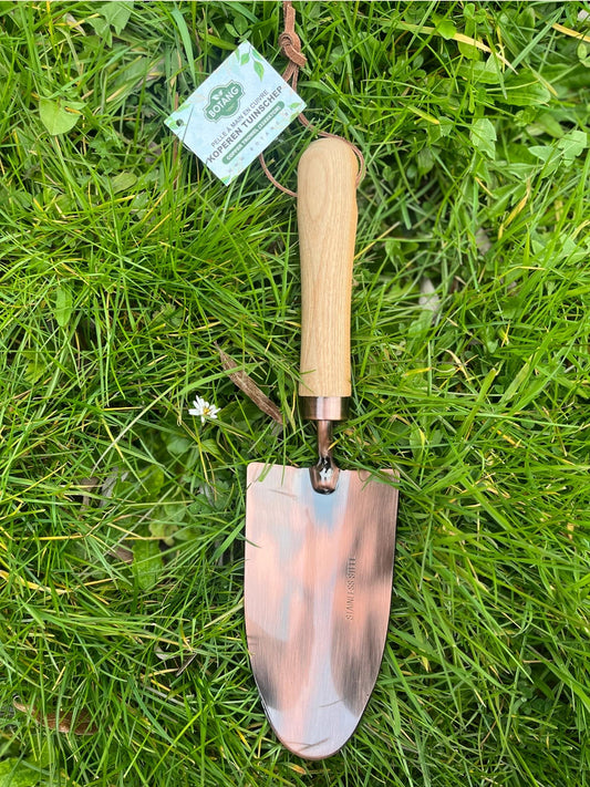 Flot haveskovl med træhåndtag og kobberbelagt skaft, der ligger på en grøn græsplæne