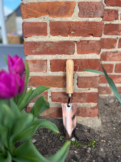 Kobberbelagt planteskovl med træhåndtag stående op ad en mur